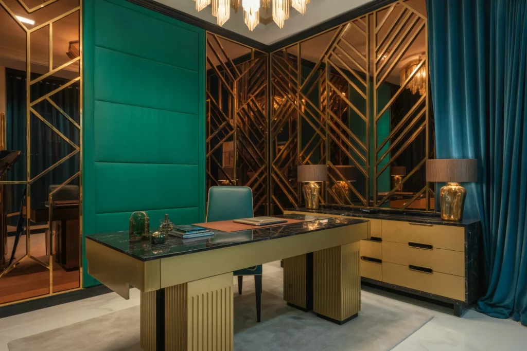 A luxurious home office with a sleek desk, gold accents, and teal walls. The space features mirrored panels, elegant lighting, and blue curtains, creating an opulent and sophisticated atmosphere.