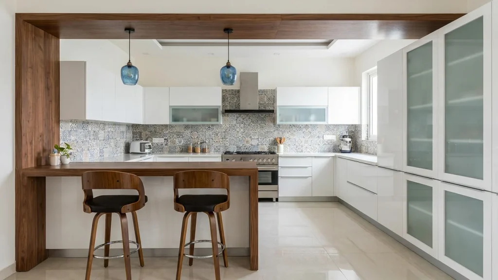 Modern kitchen with a clean and functional design, showcasing some of the best kitchen renovation ideas. It features white cabinetry, a stainless steel range, and a sleek black and blue patterned backsplash. The kitchen includes a wooden breakfast bar with two stylish bar stools, offering an open and inviting space. The layout is designed to optimize space and comfort, with ample countertop space and floor-to-ceiling storage cabinets. Natural light filters in through the window, brightening the light beige flooring and enhancing the contemporary feel of the kitchen.